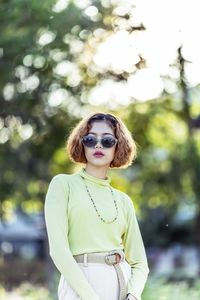 Portrait of young woman wearing sunglasses while standing against tress