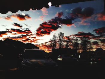 Silhouette trees against sky seen through car windshield during sunset