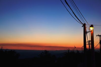 Low angle view of silhouette electricity pylon against clear sky