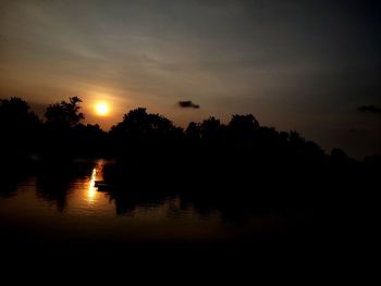 Silhouette trees by lake against sky during sunset