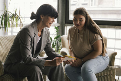 Businesswoman discussing over placard with non-binary professional while sitting at office