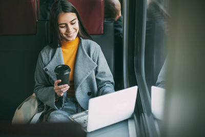 Freelance girl drinks coffee and sits on the train with a working laptop. modern technologies 