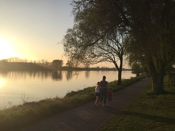 Rear view of women walking on footpath by lake against sky