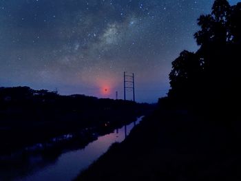 Silhouette trees by lake against sky at night