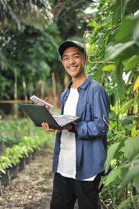 Young asian farmer man holding laptop at the garden