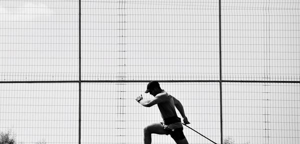 Panoramic view of male athlete running against metallic fence