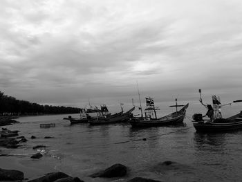 Boats in calm sea against cloudy sky