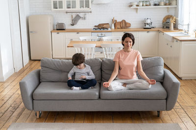 Full length of mother meditating while sitting by son at home