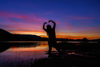 Woman showing heart symbol on hands during sunset at the lake or river, love freedom concept.