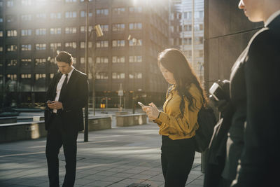 Three people standing in square using smartphones