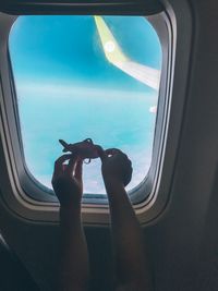 Cropped hands of child holding toy against airplane window
