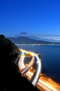 High angle view of light trails on road by sea against sky at night