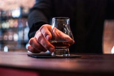 Close-up of man holding whiskey glass on table in bar