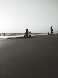 Silhouette people at mobor beach against clear sky during sunset