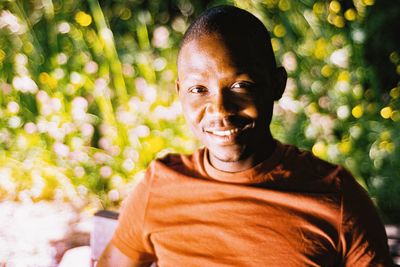 Portrait of smiling young man from ghana sitting against plants