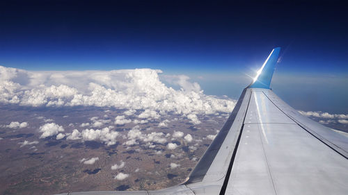 Aerial view of aircraft wing over landscape against blue sky