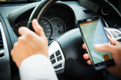 Businessman touching and using smartphone for online chat in front of steering wheel at front seat 