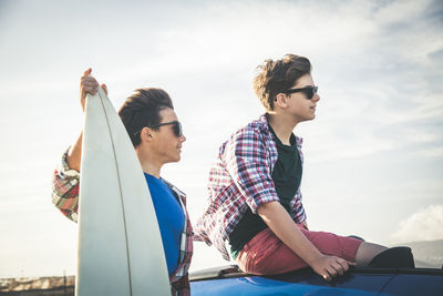 Teenage boys by car at beach against sky