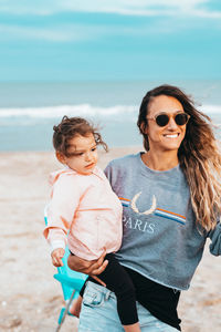 Happy woman carrying daughter while standing beach