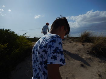 Rear view of woman standing at beach against sky