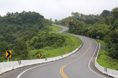 Road amidst trees and plants against sky