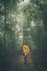 Woman with umbrella standing at forest