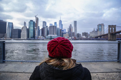 Rear view of woman looking at river by buildings against sky