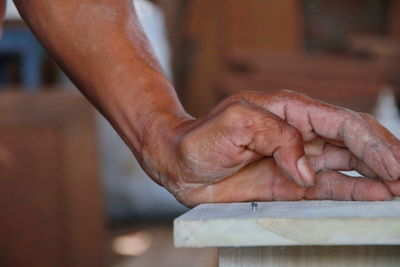 Cropped hand by nail mounted in wooden plank