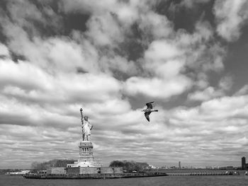Seagull flying over statue against cloudy sky