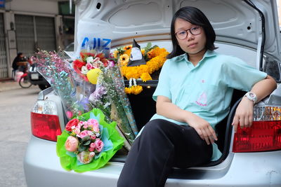 Portrait of young woman with bouquets sitting in car trunk