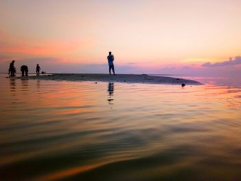 Silhouette people standing on beach against sky during sunset