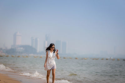 Mid adult woman wearing sunglasses walking at beach against clear sky