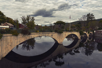 Arch bridge over river by buildings against sky