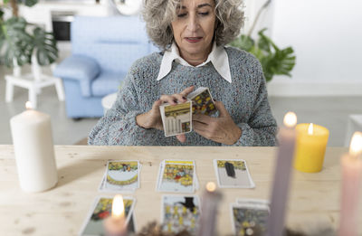 Senior woman reading tarot cards on table at home