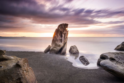 Rocks on beach against sky during sunset