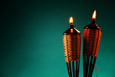 Close-up of illuminated tiki torches against green background