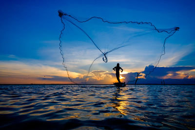 Silhouette person on sea against sky during sunset