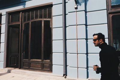 Side view of man walking with drink against building in city