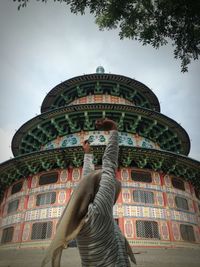 Low angle view of woman standing by building against sky