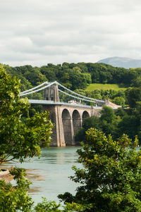 Menai bridge over river against cloudy sky