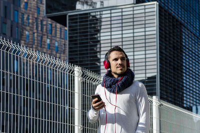 Low angel view of man wearing headphones standing against building