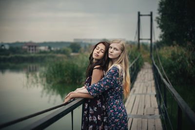 Lesbian couple embracing on footbridge against sky