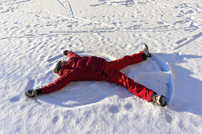 Young man in red winter clothes lying in the snow and making a snow angel. winter fun, christmas 