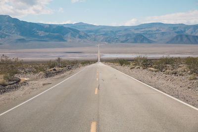 Empty road by desert against sky