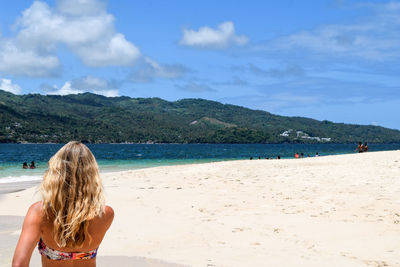 Rear view of woman standing at beach against sky