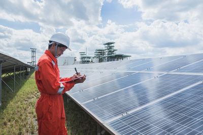 Engineer standing amidst solar panel against cloudy sky