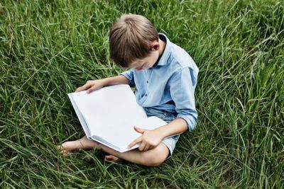 Boy sitting on book in field