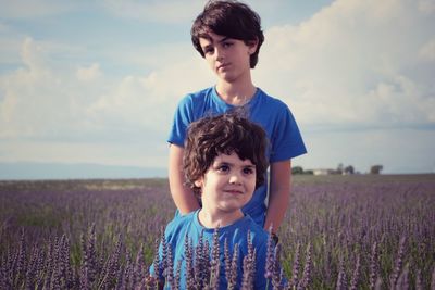 Cute siblings standing on field against sky