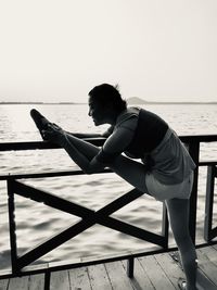 Woman stretching on pier over sea against clear sky