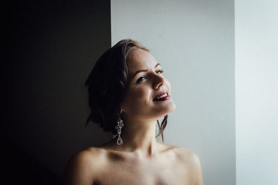 Close-up of thoughtful young woman smiling against wall